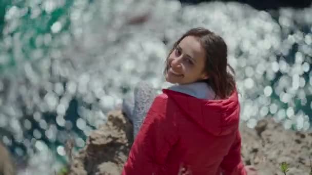 Portret Szczęśliwej Młodej Kobiety Podróżującej Jasnoczerwonej Kurtce Siedzącej Krawędzi Klifu — Wideo stockowe