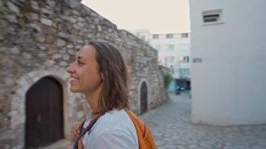 Sırt çantalı, gülümseyen güzel turist kadın turist şehrin eski turistik bölgesinde boş bir sokakta yürüyor ve Türkiye 'nin Marmaris kentinde tatilin tadını çıkarıyor. Popüler turizm merkezini gezmek