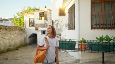 Sırt çantalı, gülümseyen güzel turist kadın turist şehrin eski turistik bölgesinde boş bir sokakta yürüyor ve Türkiye 'nin Marmaris kentinde tatilin tadını çıkarıyor. Popüler turizm merkezini gezmek