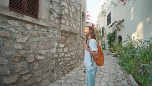 スローモーショントルコのMarmarisで休暇を楽しんでいる都市の古い観光地で空の通りを歩いてバックパックを持つ美しい女性観光客の旅行者を笑顔 人気の観光地での観光 — ストック動画