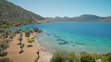 Turkuaz suyu ve cennet gibi boş deniz plajları olan güzel körfezin kıyısında turuncu elbiseli çekici, bronz tenli kadın gezgin duruyor. Kız Türkiye 'nin Marmaris bölgesinde deniz kıyısında yürüyor