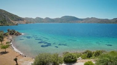 Turkuaz suyu ve cennet gibi boş deniz plajları olan güzel körfezin kıyısında turuncu elbiseli çekici, bronz tenli kadın gezgin duruyor. Kız Türkiye 'nin Marmaris bölgesinde deniz kıyısında yürüyor