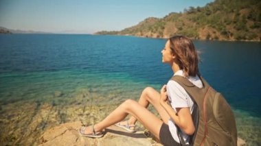 Sırt çantalı çekici, ince kadın gezgin turkuvaz suyu ve cennet gibi boş deniz plajlarıyla güzel bir deniz koyunda yürüyor. Ağır çekim 4k, Türkiye 'de seyahat