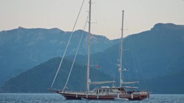 Günbatımında berrak ve turkuaz suyla körfeze demir atmış bir yat. Marmaris limanında yelkenli yatı, Türkiye. Denizi ve dağları olan güzel bir yer.
