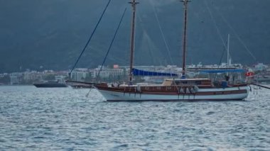 Günbatımında berrak ve turkuaz suyla körfeze demir atmış bir yat. Marmaris limanında yelkenli yatı, Türkiye. Denizi ve dağları olan güzel bir yer.