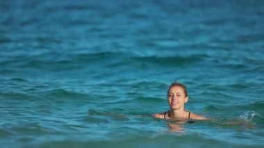 Islak siyah mayo giymiş çekici bir kadın dalgalar halinde denizin kıyısında uzanıyor..