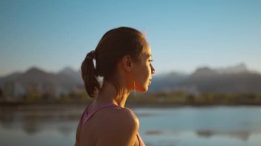 Sakin bir kadın portresi ahşap iskelede duruyor, dağlarla ve deniz manzaralı günbatımını seyrediyor. Kadın akşamdan sonra dinleniyor, nefes egzersizleri, yoga ve meditasyon.