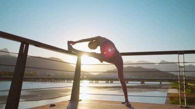 Yeni normal bir açık hava sporu, sporcu genç bir kadın dışarıda antrenmandan önce vücudunu ısıtıyor. Spor kıyafetleri giyen kız, sağlık ve refah için akşam günbatımında dışarıda egzersiz yapıyor..