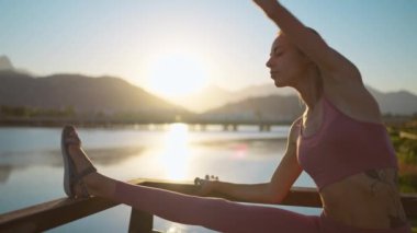 Yeni normal bir açık hava sporu, sporcu genç bir kadın dışarıda antrenmandan önce vücudunu ısıtıyor. Spor kıyafetleri giyen kız, sağlık ve refah için akşam günbatımında dışarıda egzersiz yapıyor..