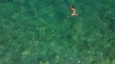 Mayo giymiş, kristal berrak suda yüzen bir kadının hava görüntüsü. Lüks seyahatler ve yaz aylarında fantastik doğa.
