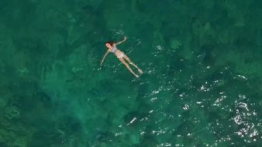 Havadan görünümü. Güzel genç kadın beyaz bikini berrak Turkuaz rengi okyanus su yüzeyinde yüzen