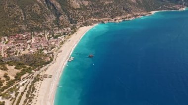 Fethiye 'deki Oludeniz yarımadasının muhteşem hava manzarası, mavi lagün, kumlu sahil üzerinde İHA uçuşu, turkuaz deniz, güneş yatakları ve şemsiyeli sahil beldesi, sıcak yaz günü..