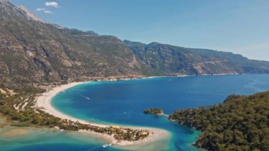 Fethiye 'deki Oludeniz yarımadasının muhteşem hava manzarası, mavi lagün, kumlu sahil üzerinde İHA uçuşu, turkuaz deniz, güneş yatakları ve şemsiyeli sahil beldesi, sıcak yaz günü..