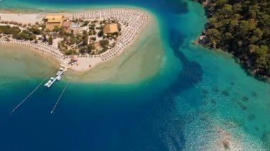 İnsanlar gök deliğinin kıyısındaki kumlu sahilde güneşleniyor. Türkiye 'nin Oludeniz kenti yakınlarındaki Akdeniz' deki gök mavisi suyun havadan görünüşü. Tekne en saf turkuaz sularda yüzüyor.