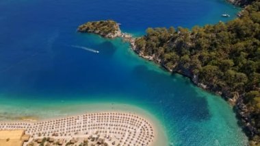 İnsanlar gök deliğinin kıyısındaki kumlu sahilde güneşleniyor. Türkiye 'nin Oludeniz kenti yakınlarındaki Akdeniz' deki gök mavisi suyun havadan görünüşü. Tekne en saf turkuaz sularda yüzüyor.