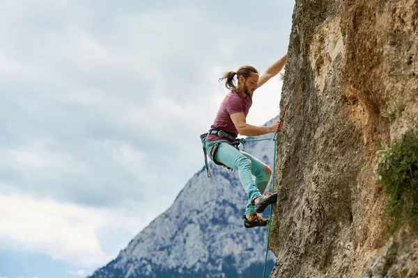 サイドビューの強い男ロープで垂直方向の岩の上に登山に集中し 登山をリード 崖の上の挑戦的なルートの作業 背景の美しい山の景色 — ストック写真