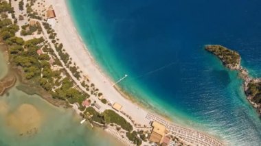 Fethiye 'deki Oludeniz yarımadasının muhteşem hava manzarası, mavi lagün, kumlu sahil üzerinde İHA uçuşu, turkuaz deniz, güneş yatakları ve şemsiyeli sahil beldesi, sıcak yaz günü..