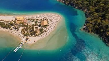 İnsanlar gök deliğinin kıyısındaki kumlu sahilde güneşleniyor. Türkiye 'nin Oludeniz kenti yakınlarındaki Akdeniz' deki gök mavisi suyun havadan görünüşü. Tekne en saf turkuaz sularda yüzüyor.