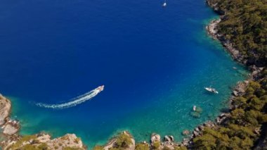 Küçük körfezdeki yelkenlilerin üzerinden uçan hava manzaralı güzel yeşil dağlara ve Türkiye 'nin Oludeniz kentindeki mavi deniz koyundaki beyaz kumlu plaja doğru. Yat, lüks tatil.