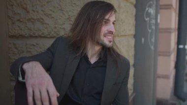 Rahatlamış genç bir adamın portresi gülümseyen ve şehir caddesinde kameraya bakan. Adam pencereye yakın oturuyor. siyah gömlek ve ceket