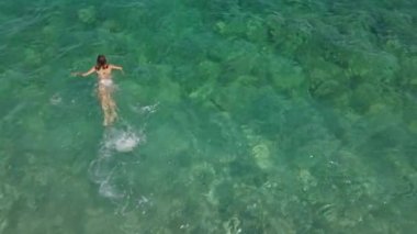 Mayo giymiş, kristal berrak suda yüzen bir kadının hava görüntüsü. Lüks seyahatler ve yaz aylarında fantastik doğa.