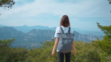 Dağın tepesindeki platformda, mavi arka plan vadisinin manzarasıyla yazı için gezen kadın turist. Moda elbiseli genç kız dağdan manzaranın tadını çıkarıyor.