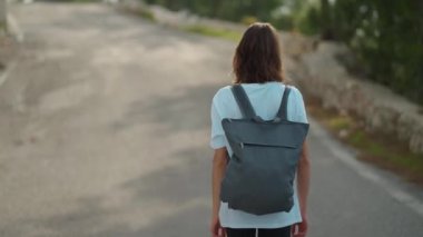 Dağın tepesinde mavi arka plan vadisi manzarasıyla yürüyen bir kadın gezgin. Günlük kıyafetler ve sırt çantalı genç turist kız dağdan manzaranın keyfini çıkarıyor.