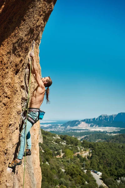 背の高い岩の上に垂直画像アスレチック男性は素晴らしい山と青い空を背景に登る — ストック写真