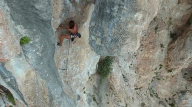 Genç, formda bir kadının hava görüntüsü kayalara tırmanma rotasında dikey uçurumda, açık havada kaya tırmanışı, yavaş çekim kaya tırmanışı anları.