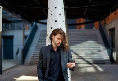 Mobil cihazlar kullanarak modern iş kavramı. Siyah takım elbiseli çekici genç bir iş adamı. Sokakta akıllı telefon kullanıyor. Her işi yapmaya hazır..