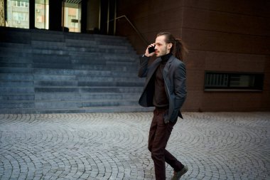 Siyah takım elbiseli genç ilerici iş adamının telefonda konuşurken caddede yürümesi. İş ve elektronik ile ilgili ticari projeler için mükemmel.