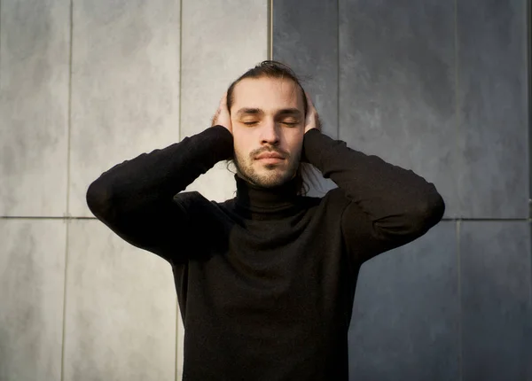Young man with closed eyes covering his ears in an effort to block out the sound around him. Conceptual image of struggle with deafness and feeling disconnected from society
