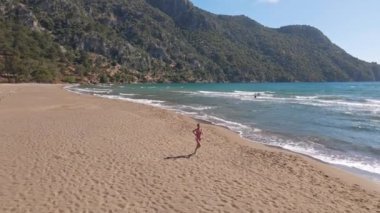 Arterial drone görüşü. Genç kadınlar açık havada egzersiz yapıyor. Deniz ve dağ arka planlarıyla koşuyorlar. Türkiye 'de yaz mevsiminde güneş doğduğunda, sağlıklı koşu ve açık hava egzersizi kavramını benimseyin.