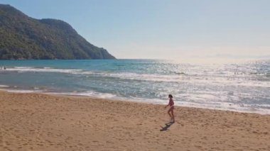 Arterial drone görüşü. Genç kadınlar açık havada egzersiz yapıyor. Deniz ve dağ arka planlarıyla koşuyorlar. Türkiye 'de yaz mevsiminde güneş doğduğunda, sağlıklı koşu ve açık hava egzersizi kavramını benimseyin.