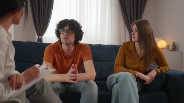 若いカップルは心理学者の前でソファに座って 彼らの関係の問題を議論し 作業する 関係の課題を克服するための専門家の助け — ストック動画