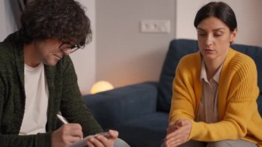 Tişörtlü ve gözlüklü yetişkin bir danışman seans sırasında kadının omzuna dokunup onu rahatlatıyor.