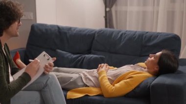 Sarı hırkalı üzgün kadın kanepeye uzanıp terapi seansında psikologla konuşuyor.