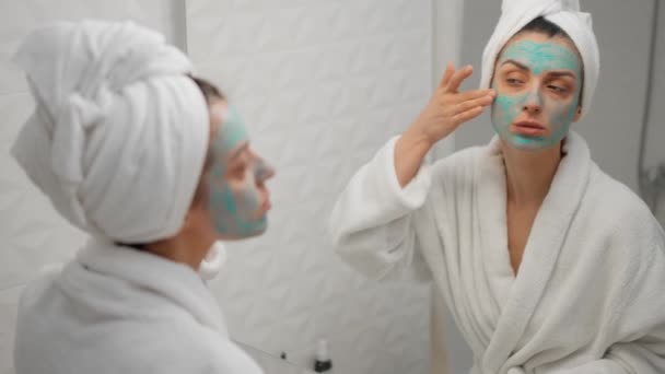 魅力的な女性は バスルームミラーで顔の表情にスキンケアクリームを適用します 頭の上に健康な若い女性ラップタオルは 顔のクリームを持ち上げる保湿を置きます 健康的なスキンケア治療の概念 — ストック動画