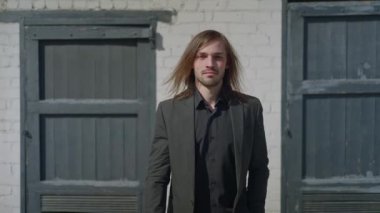 Kentin gri duvarına karşı poz veren mutlu, stil sahibi bir adam. Moda erkeği modaya uygun siyah kıyafetler giyiyor.