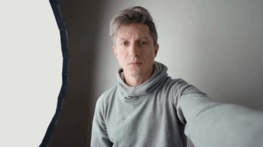 Fotoğraf stüdyosunda ışık teçhizatlı bir adam. Adam suratındaki ışığı nasıl değiştirdiğini göstermek için selfie çekiyor. vlog veya çevrimiçi fotoğraf kursu kavramı