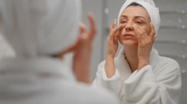Yüz yıkama ve gülümseme için nemlendirici köpük kullanan bir kadın, sabah rutini. Kaplıca salonundaki aynaya bakan kafasında havlu olan genç bir kız öğrenci. Makyaj için hazırlama