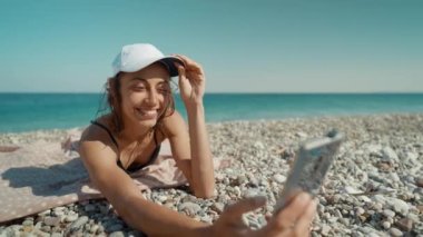 Rahat kadın turist deniz kıyısında güneşlenir, cep telefonunun kilidini açar ve fotoğraf ya da video çeker. Mavi Göl beldesi, Oludeniz, Türkiye.