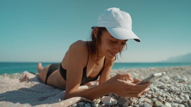 穿着比基尼的轻松自在的女性游客在靠近水边的海滩上晒日光浴 解锁她的手机 并拍照或录像 Blue Lagoon Resort Oludeniz Turkey — 图库视频影像