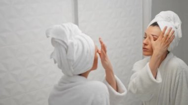 Güzel bir kadın beyaz banyoda cilt bakımı için cilde krem sürüyor.