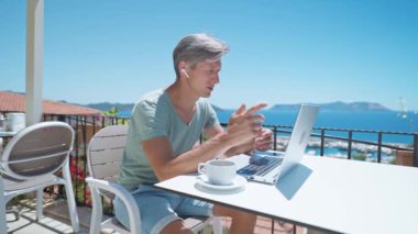 man freelancer or businessman wearing earphones holding video call, spiking with client or team during summer vacation at sea resort in Turkey. Remote work, drink coffee, go everywhere