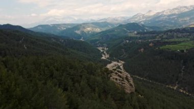 Yeşil çam ağaçlarıyla güzel manzaralı dağ sırtı, karlı dağlar ve dramatik bulutlu gökyüzü. Türkiye 'de seyahat, Tazi kanyonu bölgesinde. Sinematik İHA, 4 km yavaş çekim çekiyor.