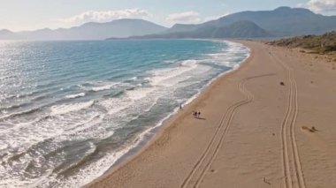 Güneş doğarken, İztuzu Kaplumbağa Sahili, Türkiye 'de tropikal beyaz kum plajı üzerinde uçan hava manzarası. Güneşli bir günde kumsalda yürüyen insanlar. Yaz tatili ve turizm
