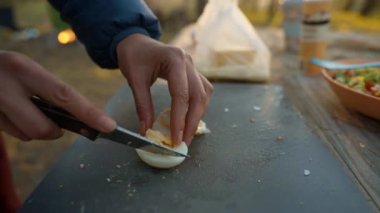 Doğada piknik. Kadın dışarıda yemek pişiriyor. Yakın plan kadın elleri günbatımında sonbahar ormanında salata için yumurta kesiyor. Hafta sonu gezisi ve doğada kamp.