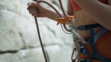 Koşumlu ve iple bağlanmış dişi atletik kaya tırmanışçısı bir ip tutuyor. Sporcu kızda tırmanma ekipmanı var. Dişi dağcı, dağa tırmanırken partnerini bağlar. Uçurumun kenarına tırman