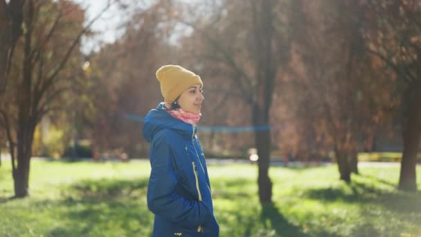 在阳光明媚的日子里 穿着黄色便帽的女人站在秋天的公园里 绿树成荫 秋天和大自然中的人 积极休闲 — 图库视频影像